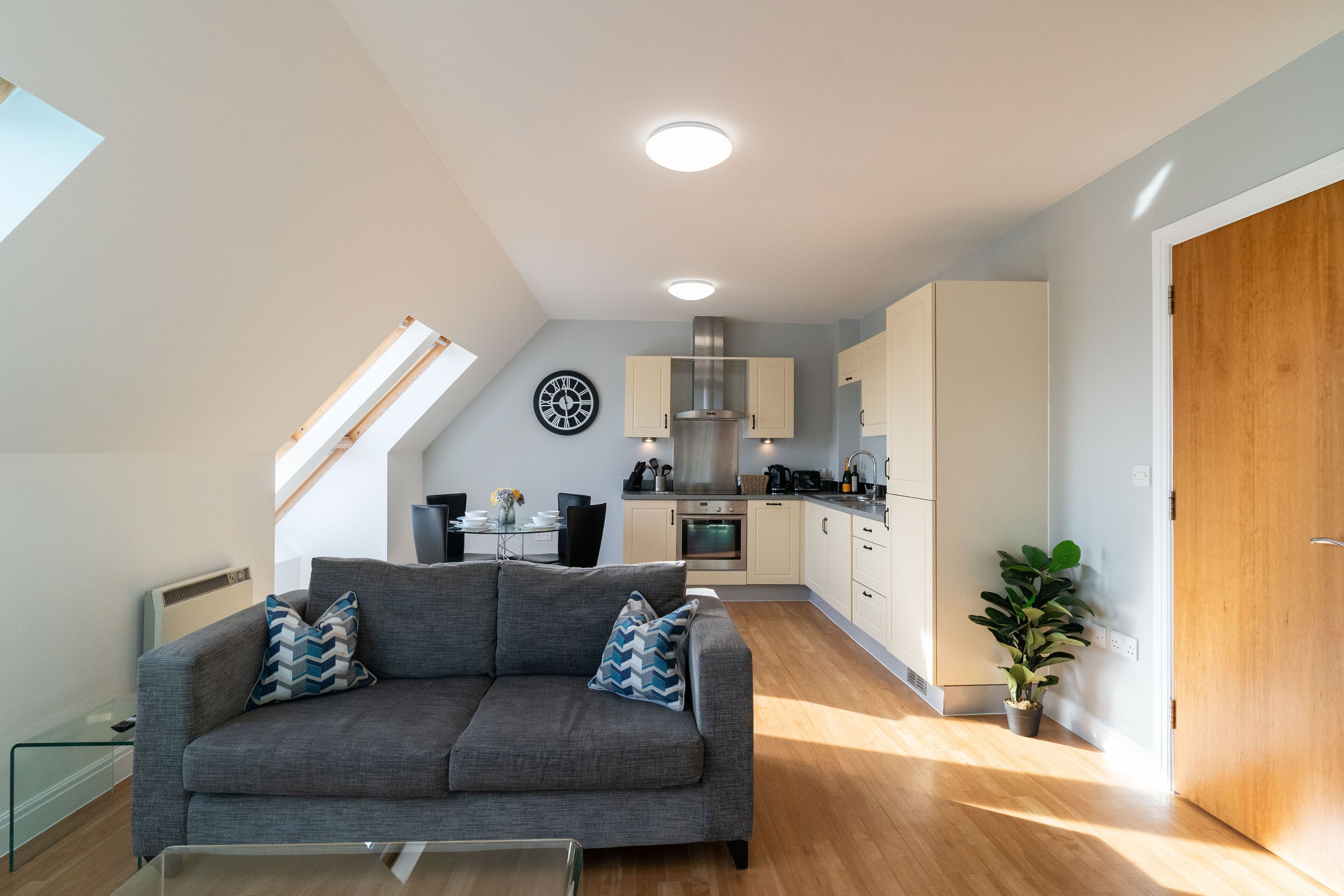 Un appartement moderne avec un canapé gris, un coin repas, une cuisine et une porte en bois.
