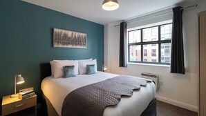 Habitació d'hotel ben ordenada amb un llit gran, una taula de nit amb una làmpada, una finestra amb cortines i una obra d'art penjada a la paret.