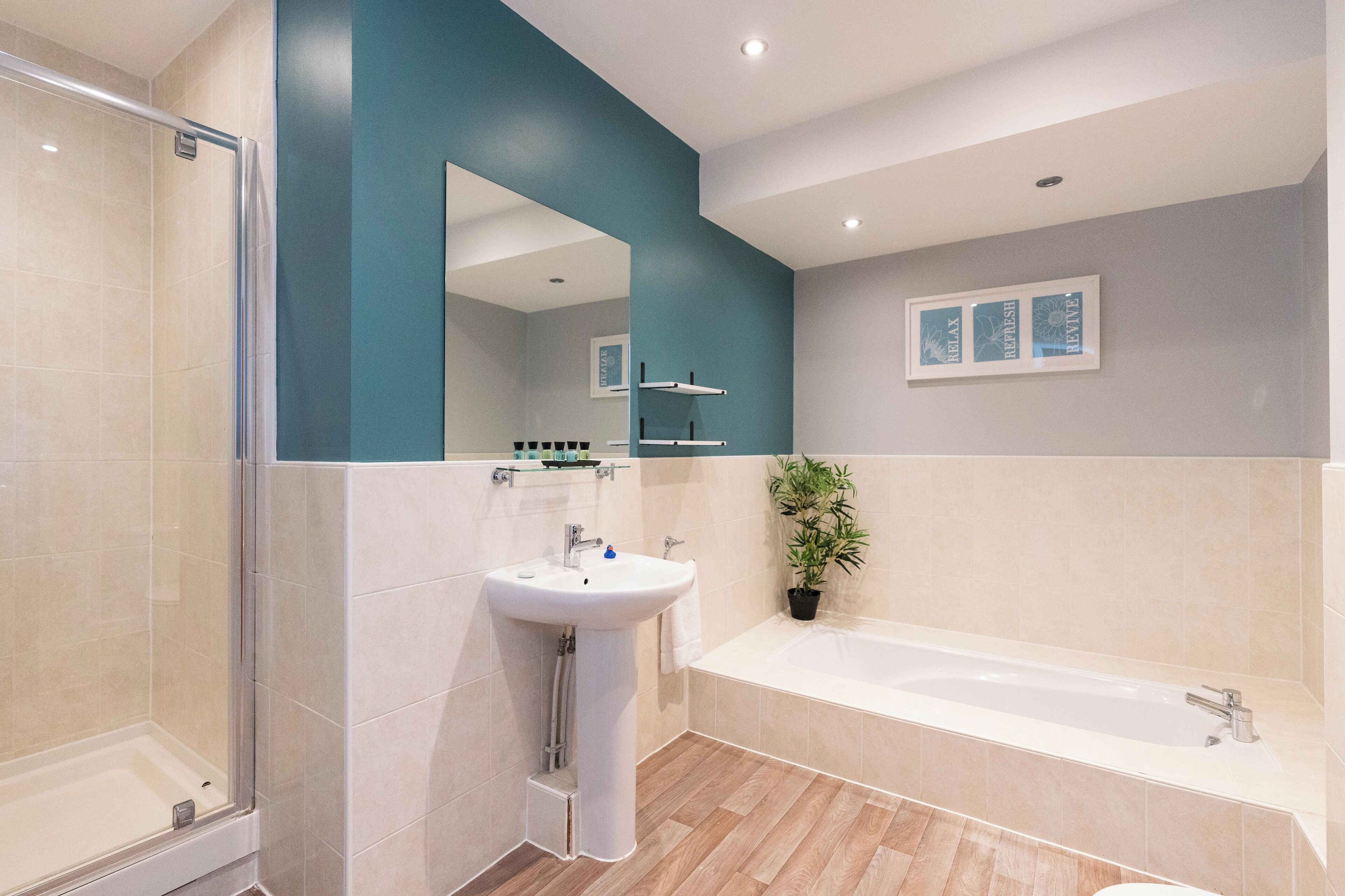 Ein modernes Badezimmer mit Duschkabine aus Glas, einem Standwaschbecken, einer Badewanne und einer Topfpflanze.