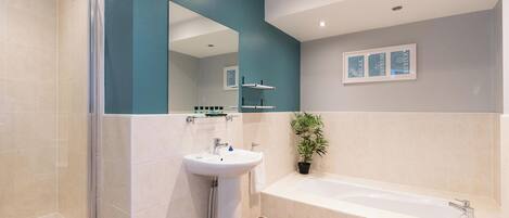 A modern bathroom with a glass shower enclosure, a pedestal sink, a bathtub, and a potted plant.