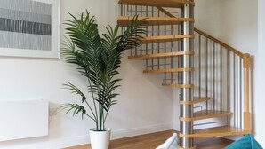 Una escala amb graons de fusta, baranes metàl·liques, una planta en test i una obra d'art emmarcada a la paret.