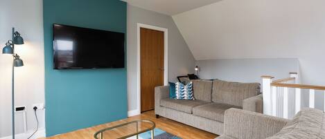 A modern living room with a teal accent wall, a flat-screen TV, a sofa, a coffee table, and a staircase.