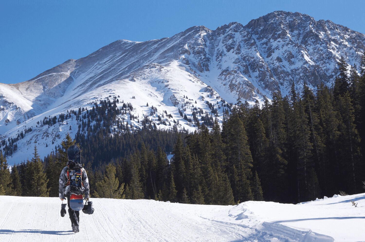 A snowboarder descending a snowy slope with a mountain in the background.