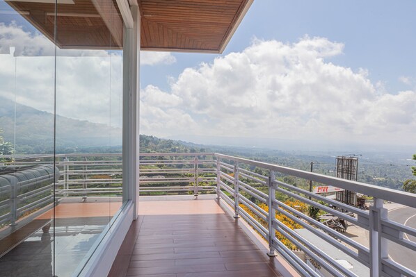 A balcony with a clear view of a mountainous landscape, a paved floor, and a metal railing.