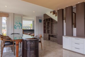 A modern kitchen with a dining area, featuring a glass table, wooden chairs, and a view of the outdoors.