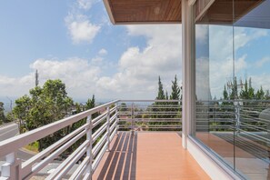 A balcony with a wooden floor and metal railing overlooking a cityscape with trees and buildings.
