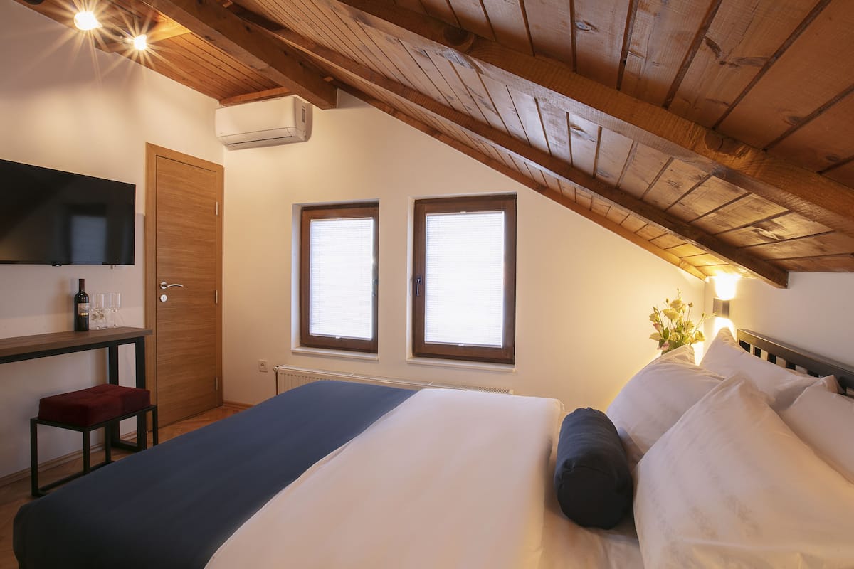 Une chambre à coucher avec un lit, un bureau avec une chaise, une télévision et deux fenêtres.