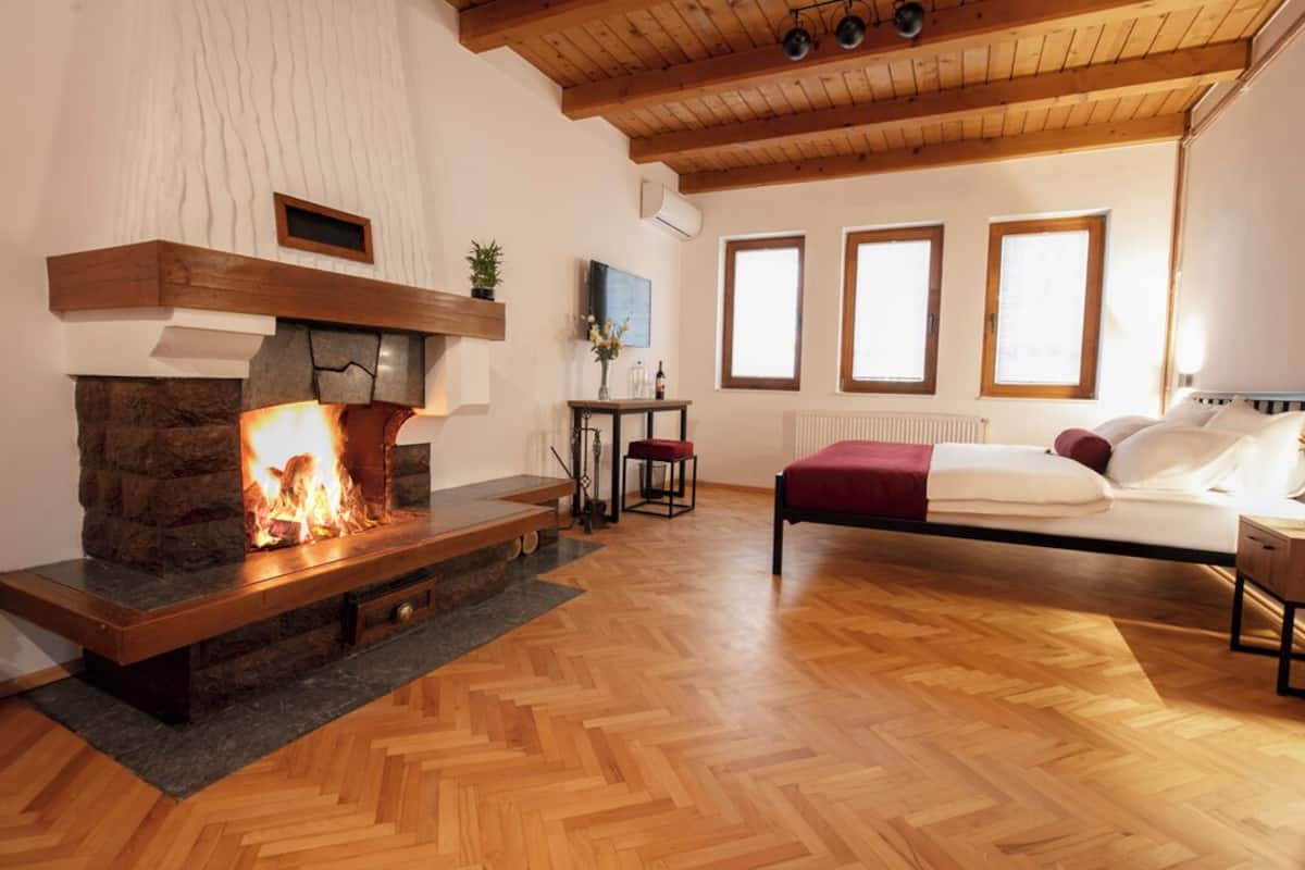 Une chambre avec une cheminée en pierre, un plancher en bois et un lit recouvert d’une couverture rouge.
