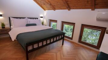 A bedroom with a wooden bed, a green mattress, a wooden headboard, a nightstand with a plant, and two windows with a view of trees.