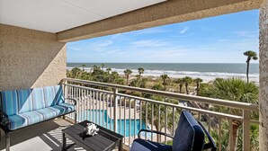Ein Balkon mit Pool, Sofa und Stuhl mit Blick auf das Meer und den Strand.
