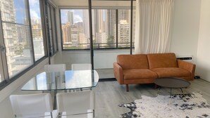 Un salon moderne avec une table en verre, des chaises blanches, un canapé orange, une table basse ronde et un tapis en peau de vache.