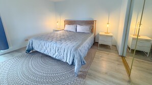 Une chambre à coucher comprenant un lit, deux tables de chevet, une commode, un grand miroir et un tapis à motifs.