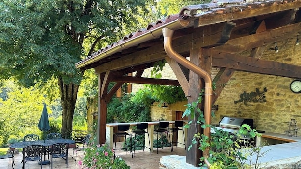 An outdoor patio with a wooden pergola, stone seating, and a barbecue area. - Stunning Dordogne Holiday House and private heated pool. (Saint-Pompont)