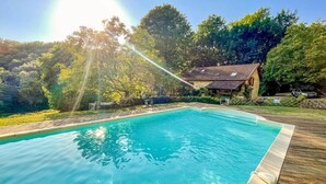 A rectangular swimming pool with a wooden deck surrounding it, set against a backdrop of trees and a house. - Stunning Dordogne Holiday House and private heated pool. (Saint-Pompont)