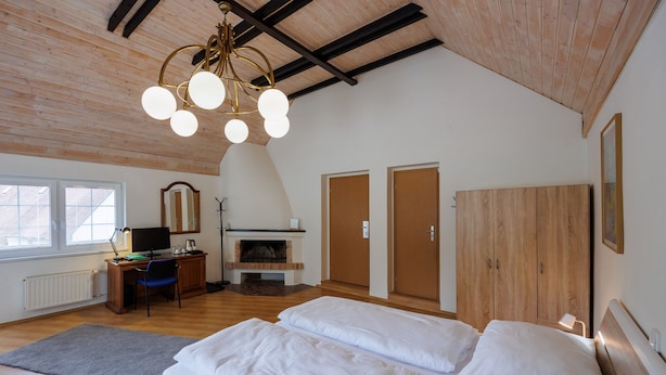 Un dormitorio con techo de madera, chimenea, un escritorio con computadora y dos camas.