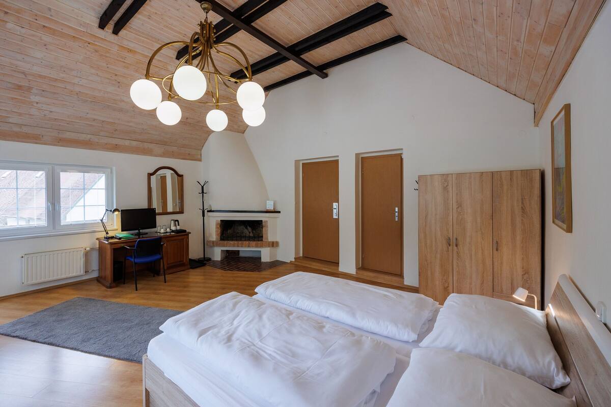 A bedroom with a wooden ceiling, a fireplace, a desk with a computer, and two beds.