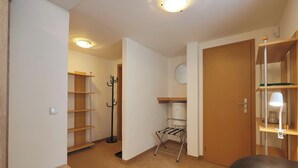 Una habitación con puerta de madera, un perchero, un tendedero de metal y una estantería con una lámpara.