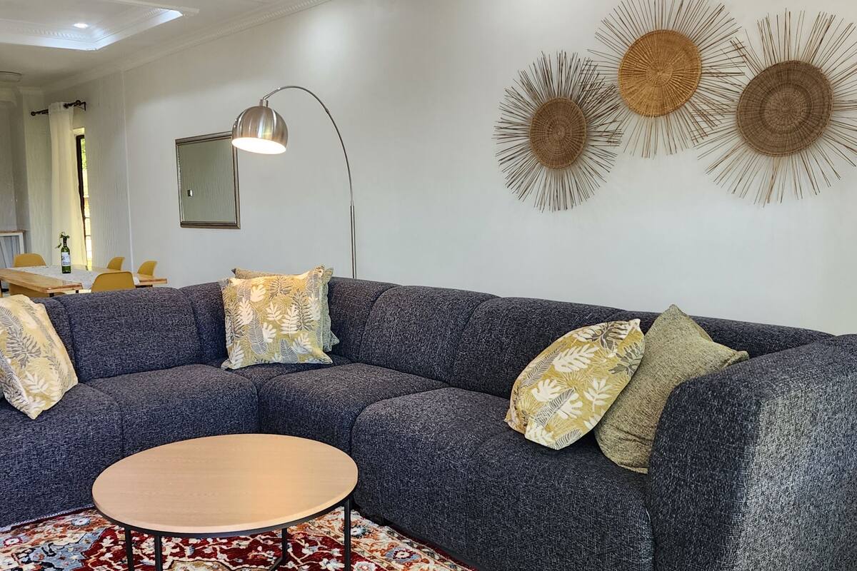 Uma sala de estar moderna com um sofá modular cinza, uma mesa de centro de madeira redonda e arte decorativa na parede.