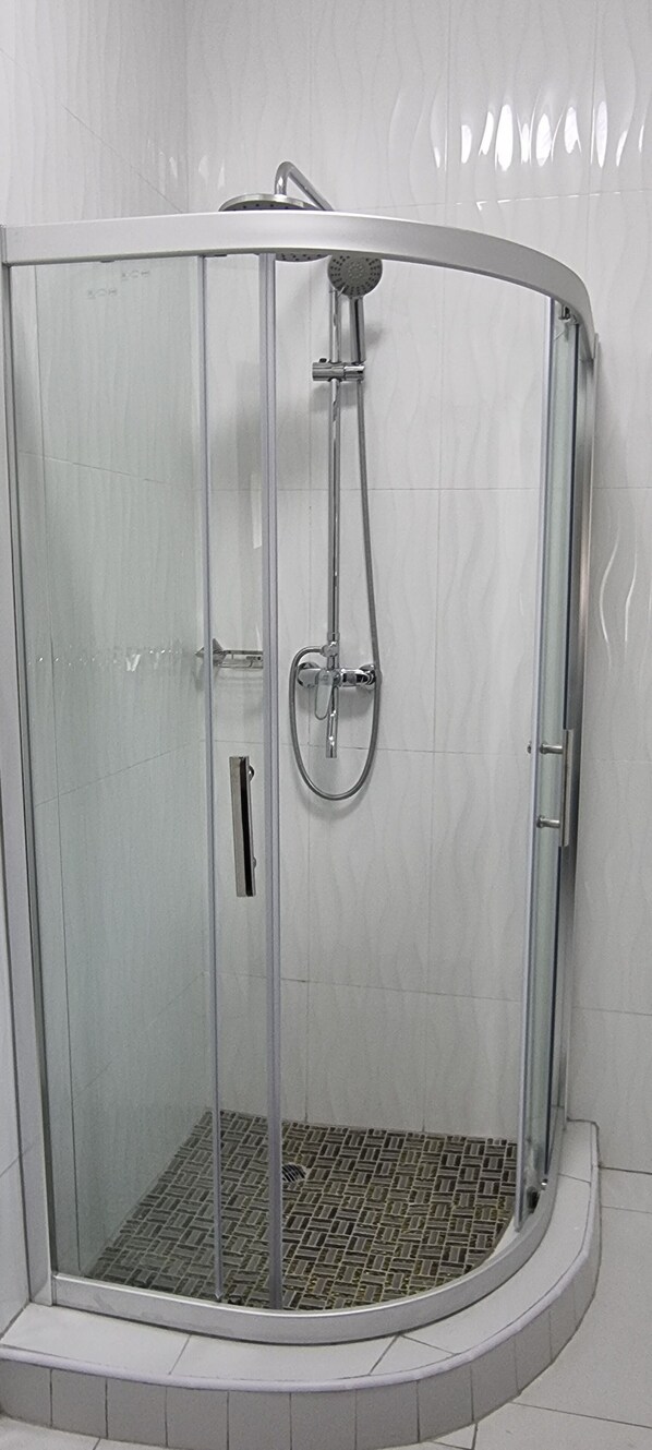 Ducha con cerramiento de vidrio, cabezal de ducha de mano y llave de control en la pared.