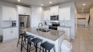A modern kitchen with white cabinets, stainless steel appliances, granite countertops, and black bar stools. - Serene 3BR w/ Private Hot Tub - Snow Canyon Views (Saint George)