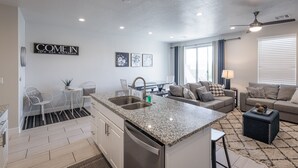 A modern kitchen with granite countertops, a built-in dishwasher, and a dining area with a small table and chairs. - Serene 3BR w/ Private Hot Tub - Snow Canyon Views (Saint George)