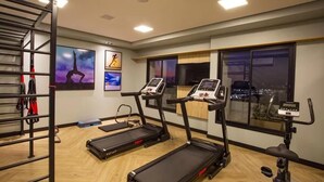 A gym with treadmills, an elliptical, and a stationary bike. There are exercise mats and a rack with equipment.