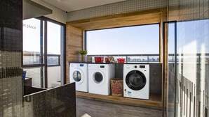 A modern laundry room with three washing machines, a large window with a city view, and a wooden ceiling.