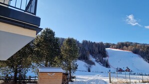 Paisaje nevado con una cabaña de madera, una pista de esquí y un edificio con tejado inclinado.