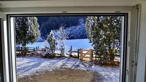 Una ventana con vista a un paisaje nevado, que incluye árboles y una valla de madera.