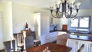 Un comedor con mesa de madera, armarios blancos, sillas de mimbre y una araña.