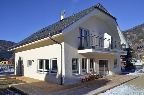 Ein zweistöckiges Haus mit Balkon, großen Fenstern und einer Holzterrasse.