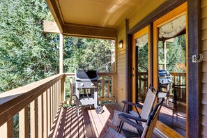 Eine Holzterrasse mit Grill und Stühlen, mit Blick auf eine bewaldete Landschaft.
