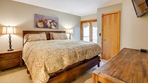 A bedroom with a large bed, two bedside tables, a wooden desk, a painting on the wall, and a door with a window. - Winter Park Condo w/ Sleeping Loft - Near Main St (Winter Park)
