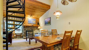 A wooden dining table with chairs, a spiral staircase, and a stone fireplace. - Winter Park Condo w/ Sleeping Loft - Near Main St (Winter Park)