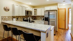 A kitchen with white cabinets, a granite countertop, a stainless steel refrigerator, and a microwave. - Winter Park Condo w/ Sleeping Loft - Near Main St (Winter Park)