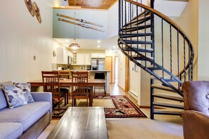 Ein geräumiger Wohnbereich mit Sofa, Esstisch, Stühlen, einer Treppe und einer Küche im Hintergrund.