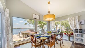 A dining area with a table set for six, large windows with a view of the water, and a kitchen area with a microwave and cabinets. - Beautiful Marble Falls Getaway on Lake Lbj! (Marble Falls)