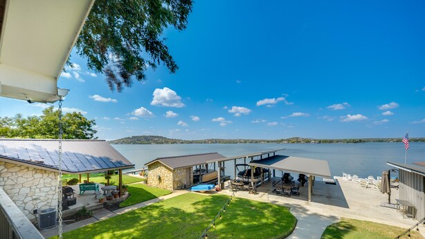 A lakeside patio with a covered seating area, stone building, and a flag. - Beautiful Marble Falls Getaway on Lake Lbj! (Marble Falls)