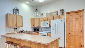 Una cocina con armarios de madera, una isla grande con taburetes, un microondas, un refrigerador y un cartel que dice 'Relax'.
