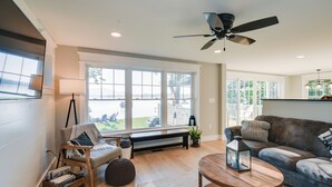 A spacious living room with a large window, a ceiling fan, a wooden coffee table, and a cozy seating area. - Lakefront Center Ossipee Home w/ Boat Dock! (Center Ossipee)