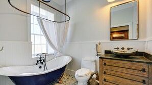 Une salle de bain avec une baignoire sur pieds, des toilettes, un meuble-lavabo en bois avec un lavabo intégré et un miroir au-dessus du meuble-lavabo.