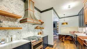 Une cuisine moderne avec un revêtement mural en motif chevrons, des meubles en bois et un îlot central doté d’une plaque de cuisson intégrée.