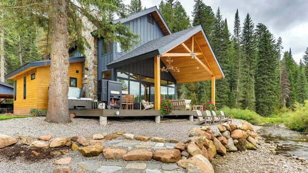 A modern log cabin with a stone foundation, large windows, and a covered porch with outdoor seating. - Modern Turnerville Cabin w/ Hot Tub & Scenic Views (Bedford)
