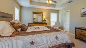 A bedroom with a bed, a dresser, a chair, a mirror, and a ceiling fan.