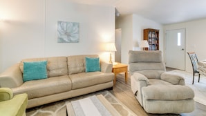 A living room with a beige sofa, a matching armchair, a small table with a lamp, and a bookshelf. - Weeki Wachee Home w/ Fire Pit: 13 Mi to Ocean! (Brooksville)
