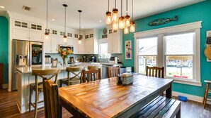 A spacious kitchen with white cabinets, a wooden dining table, and pendant lights.