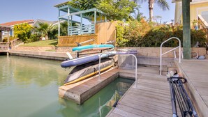 A wooden dock with a pool, kayaks, and a covered seating area.