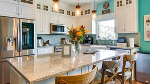 A kitchen with white cabinets, stainless steel appliances, a granite countertop, and wooden chairs.