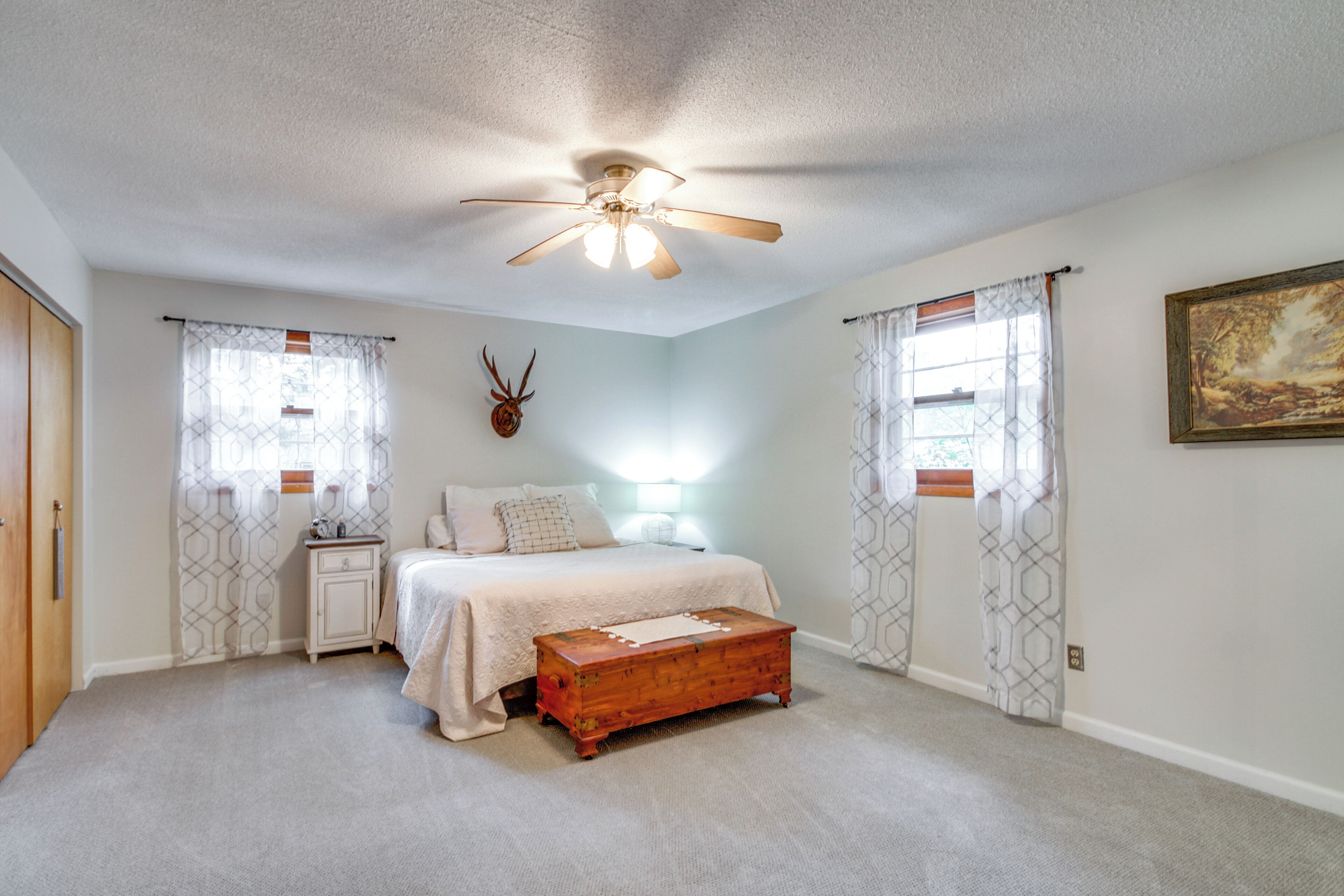 A bedroom with a bed, nightstand, wooden chest, ceiling fan, and decorative wall piece.