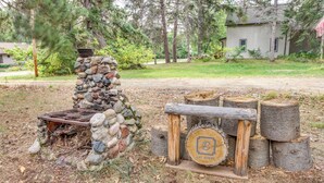 A stone fireplace with a metal grate, surrounded by logs and a wooden bench. - Pet-friendly Pequot Lakes Vacation Rental Cabin! (Pequot Lakes)